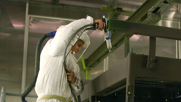 a worker powder coats some equipment in a white safety suit